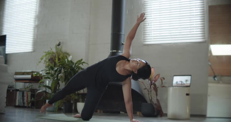 A woman following along with a workout video on a laptop in a living room at daytime