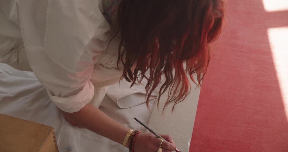 Woman squatting down on a floor painting with a paintbrush in a room at daytime