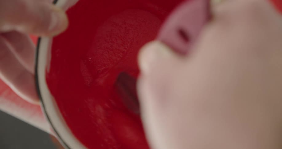 A person mixing bright red paint inside a bowl with a brush