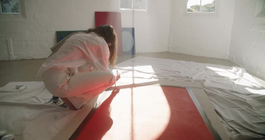 A woman kneeling and painting on a large canvas