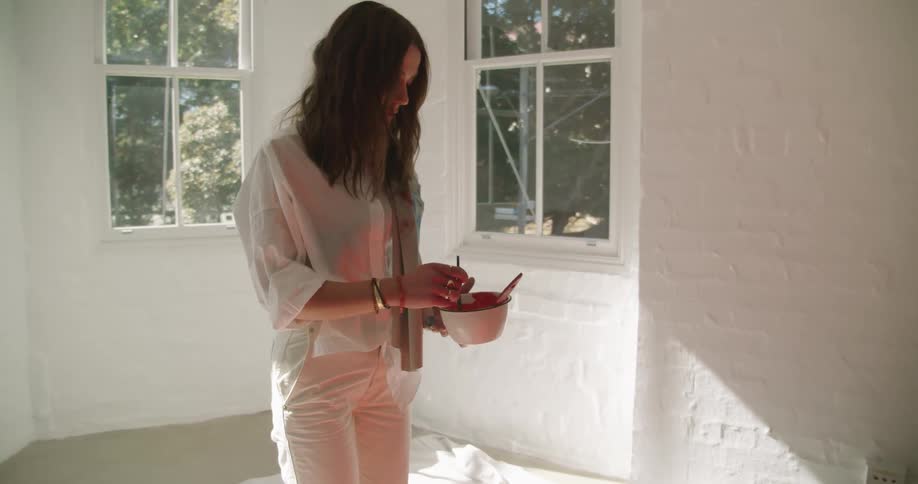 An artist holds a bowl of paint and looks down at her painting