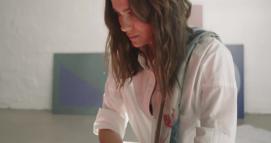 An artist holds a cup of coffee and examines her painting
