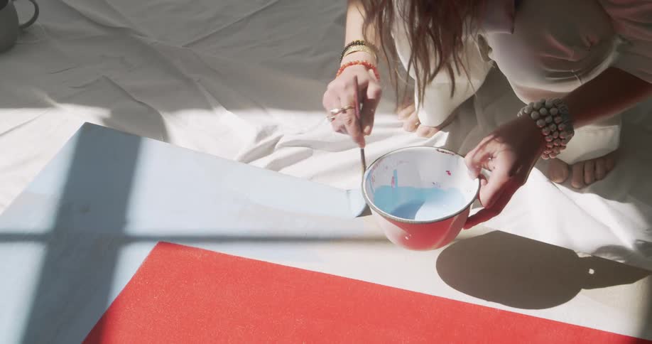 White woman painting a canvas in the floor with blue ink