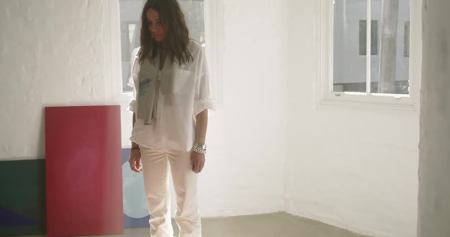 A woman wearing all white stands looking at a painting on the floor