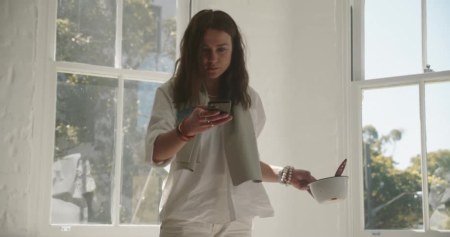 A woman holds a bowl of paint in one hand as she uses her smartphone to take a photo of the ground