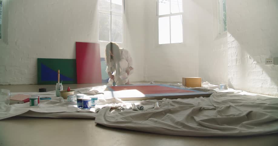 Woman paints on a canvas as she kneels on the floor