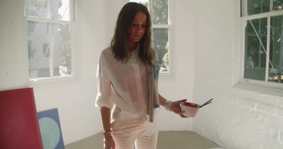A woman holds a bowl of paint and examines her artwork