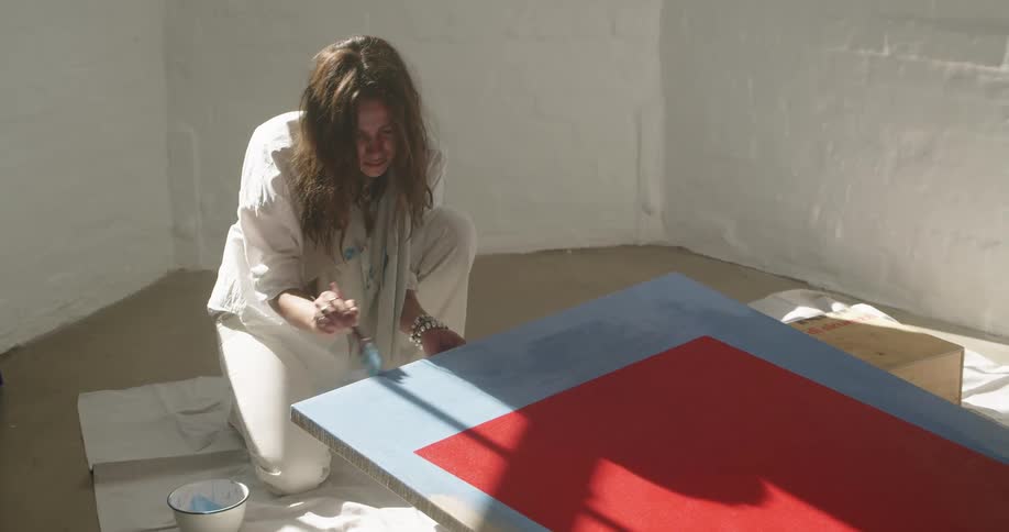 Long haired woman painting with a brush on a canvas in the floor of a room