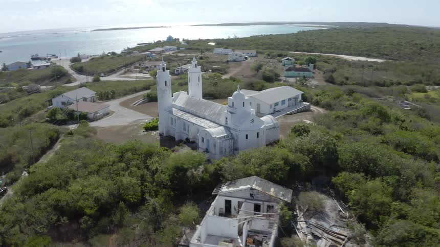 Aerial view of a white colonial church on a hill near a tropical coastal town