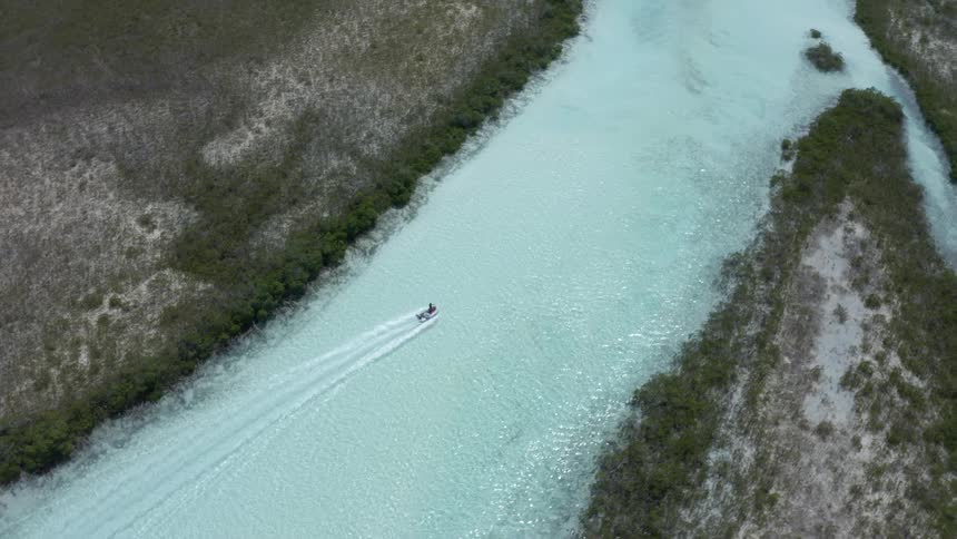 Aerial view of a small boat craft going up a clear water river at daytime