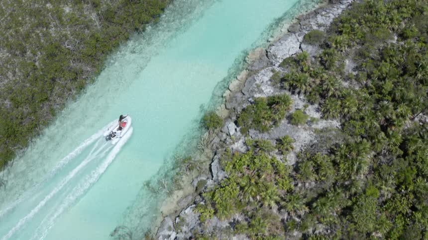 Aerial view of a man on a small river raft going upstream in between flat land with plants at daytime