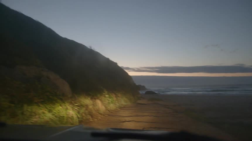 Vehicle driving over the sand near a beach at sunset