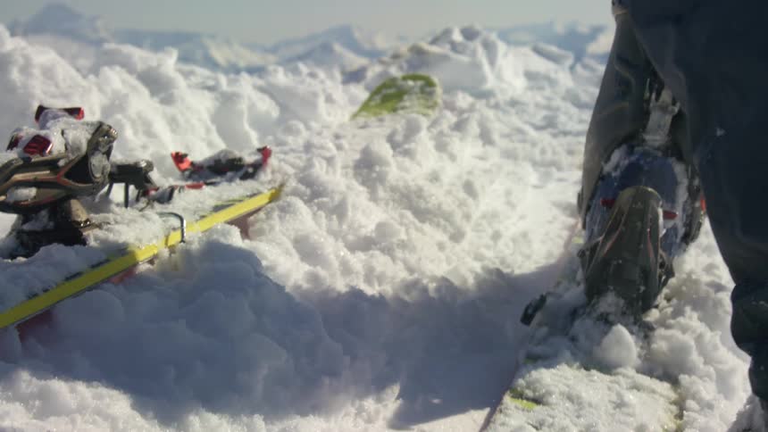 A foot pounds the snow on a ski board outdoors on a snowy mountain top