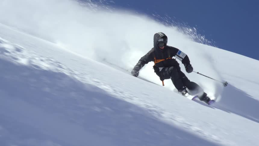 A skier sends up clouds of snow as they ski down a snowy mountain slope on a sunny day