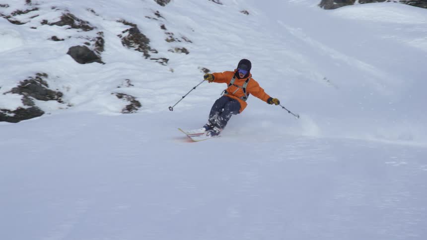 A person skiing down a mountain sprays snow as they turn