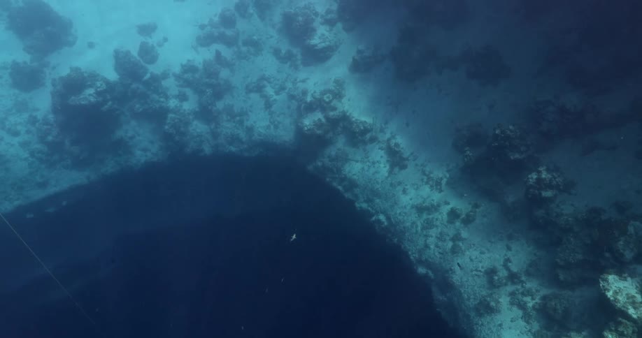 Blue Hole underwater in the ocean with small fish swimming around above it