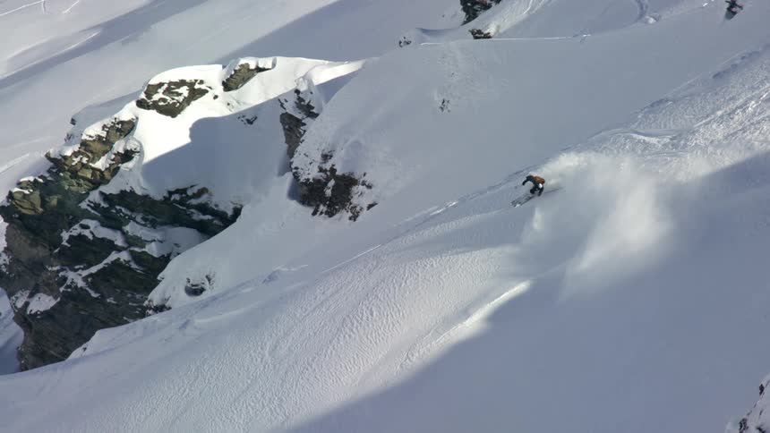 Aerial of a skier skiing down a snowy mountain on a sunny day