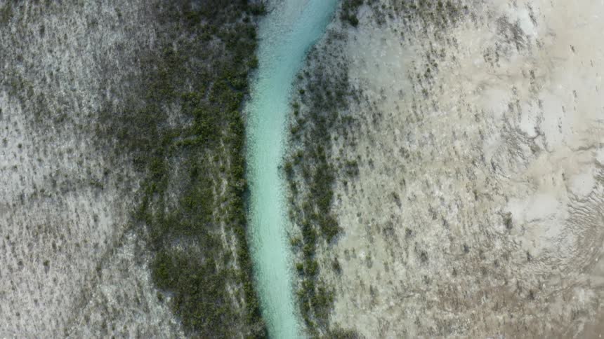 Aerial view of a river of clear light blue water running through the fields
