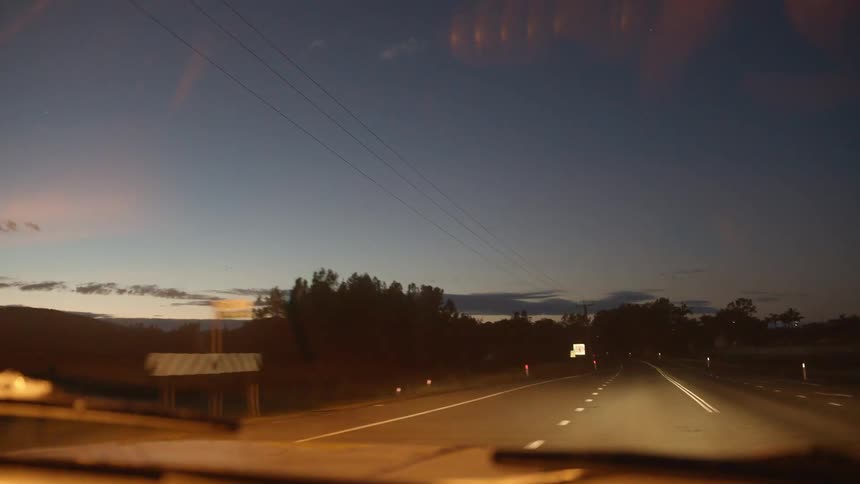 Vehicle with headlights on driving on a road through a rural area at evening