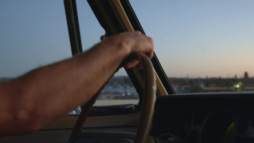 A person driving along a bridge in a vintage car in a tropical area