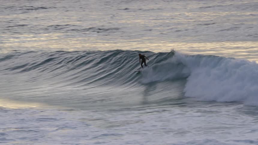 A person surfs on a wave in the ocean at dawn