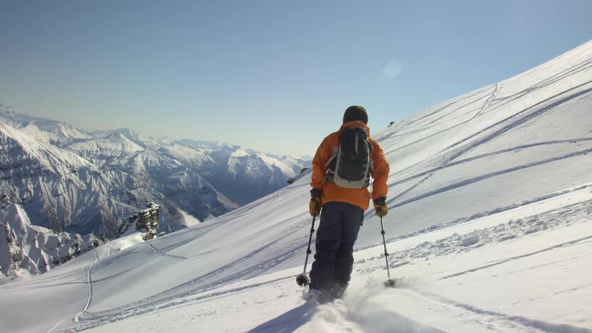 A skier makes fresh tracks on a mountain slope on a bright sunny day