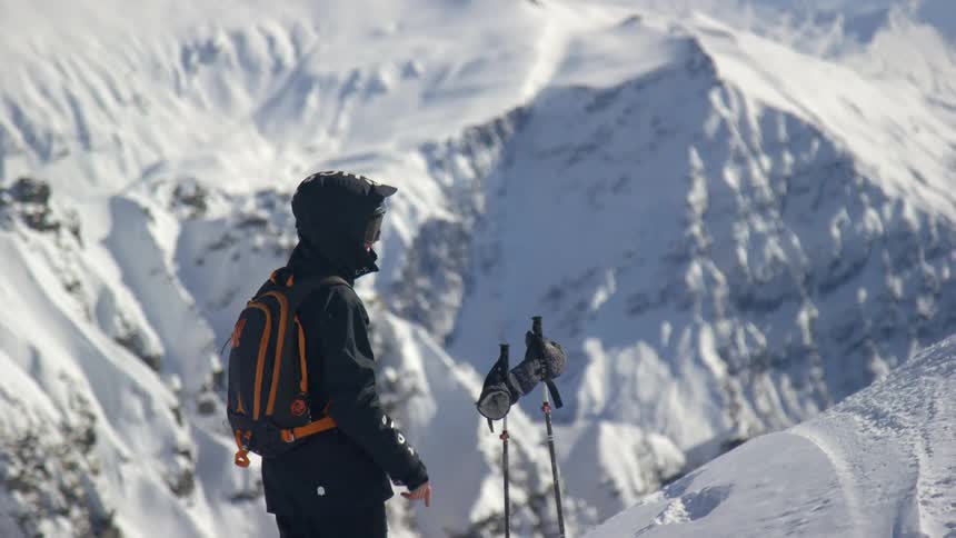 A person with a backpack and a coat standing on a snowy slope with a mountain in the background