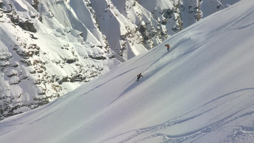 Two skiers sliding down the snow covered slope of a mountain