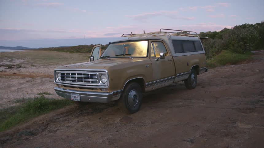 Man closing the door of a truck on a rural area next to the beach at sunset