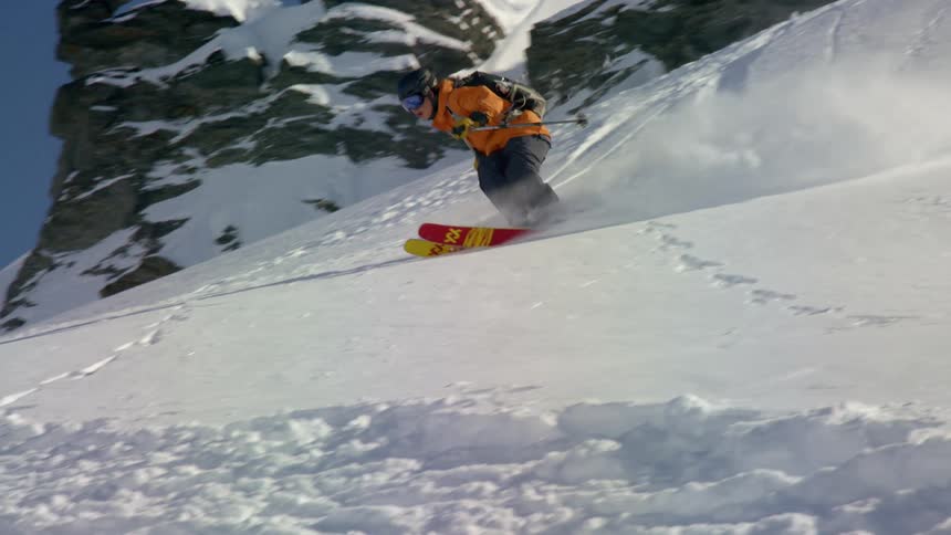 A skier descends a snowy mountain slope on a sunny day