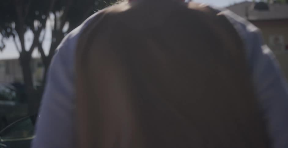 A young girl with her arms crossed angrily leans against a car and man gets out and goes to her and yells at her and grabs her face as she pulls away