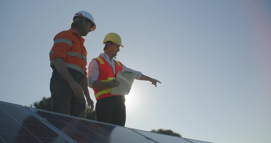Male employer discusses project with male employee while standing outdoors in sunny conditions
