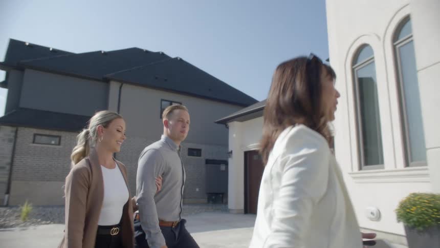 A woman holds onto her husbands arm as they follow a real estate agent to a house showing