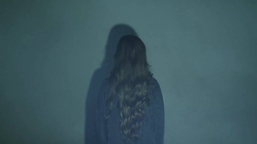 Projections over the back of a long haired blonde woman standing in front of a wall