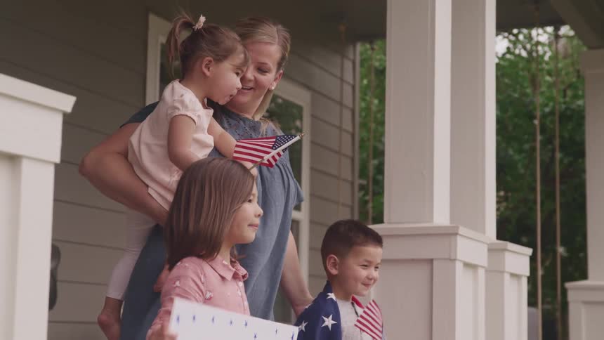 Mom and children wait outside holding american flags and a welcome home sign