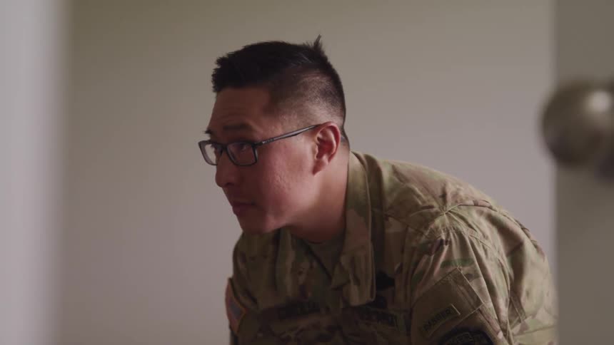 A military man with glasses and uniform sitting looking at the floor then looking up