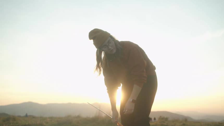 Young woman assembling a tent to camp on a mountain at sunset