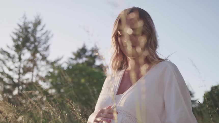 A pregnant woman embraces her stomach while posing in a field