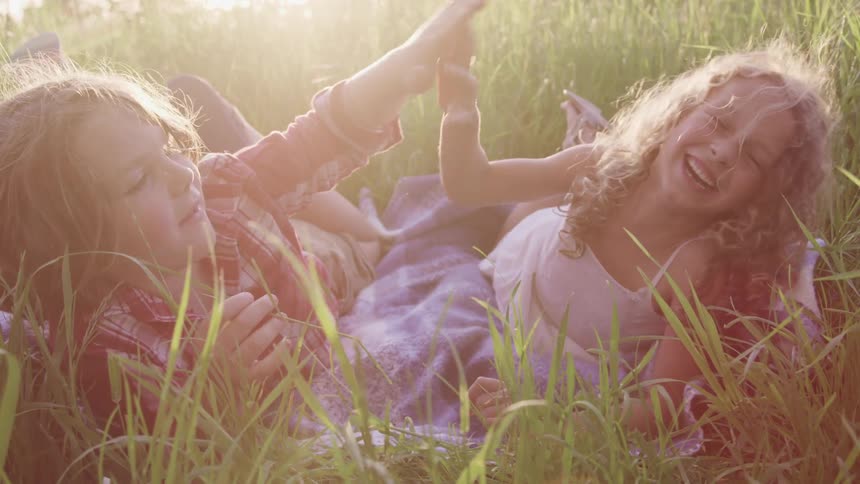 A boy and a girl laying on a blanket over the grass high five each other at sunset
