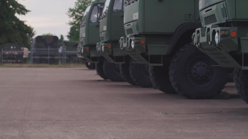 Large military trucks and vans parked in a lot at daytime