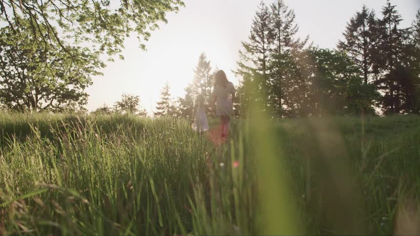 A woman and child are holding hands walking through grass