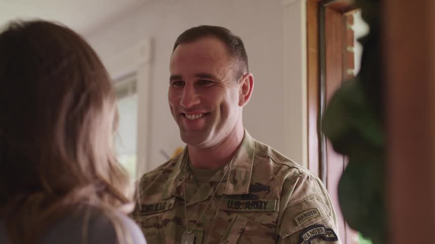 Military man hugging his wife and smiling next to the door