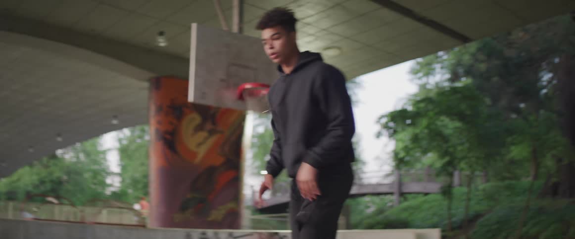 A male teenager is dribbling with a basketball in front of an outdoor hoop