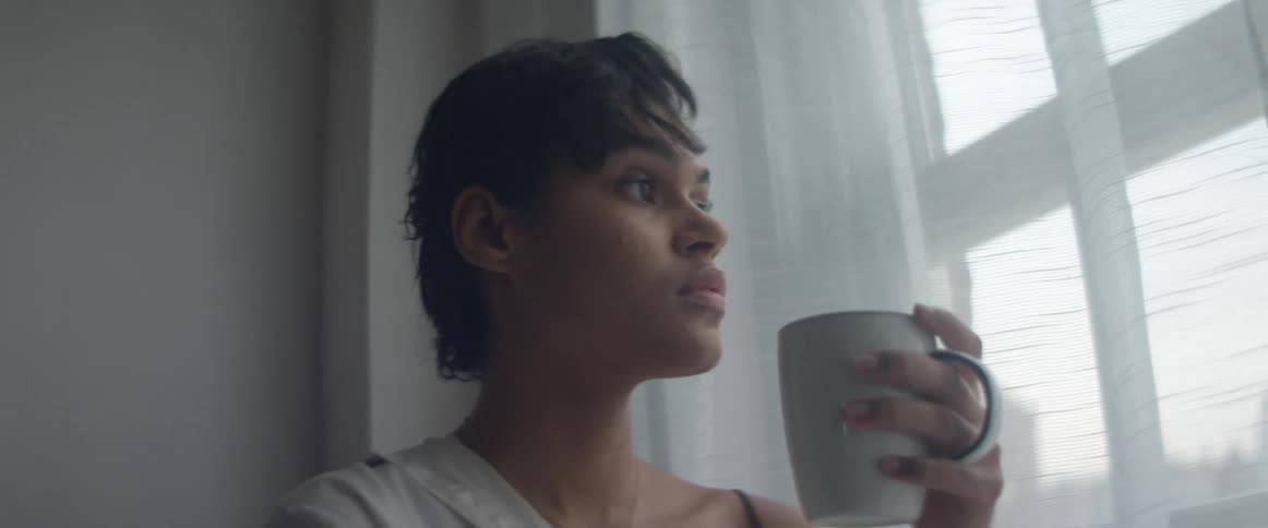 Young woman drinking a hot beverage looking out the window at home
