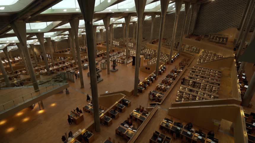 A few people walk past desks and exhibits in an empty concourse