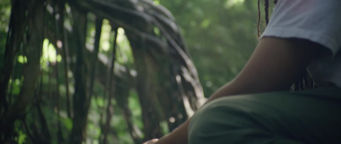 A man kneeling near a river washing a sheet of glass in the forest