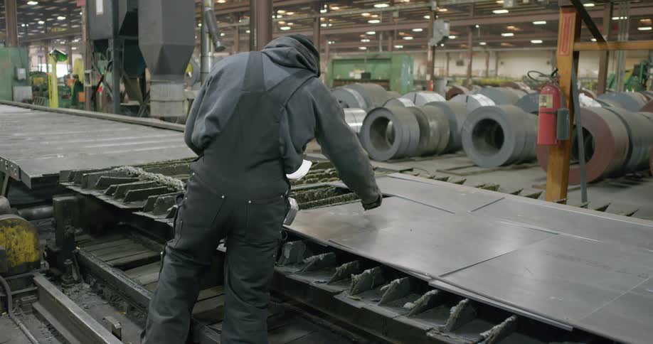 Man working in factory makes notes on sheeting while consulting paper