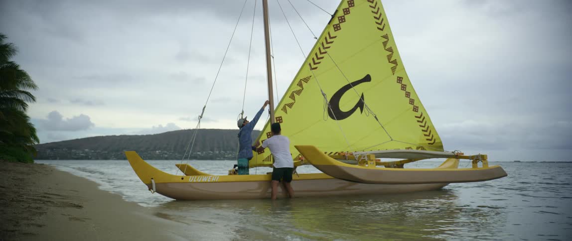 Two men lift up the sail on a sailboat near a beach
