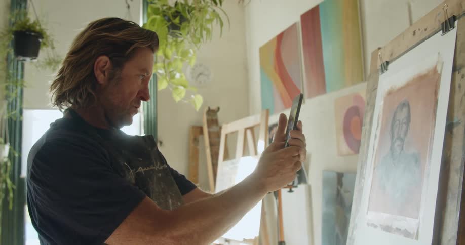A painter taking photographs of his pictures with a smartphone in a studio