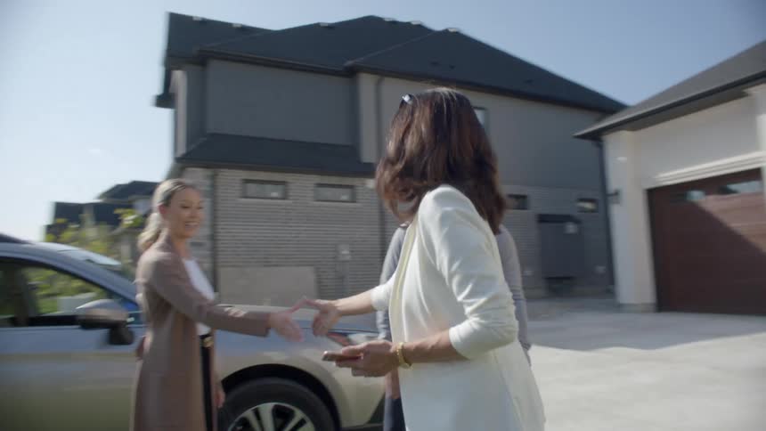 A man and woman meeting someone in front of a house